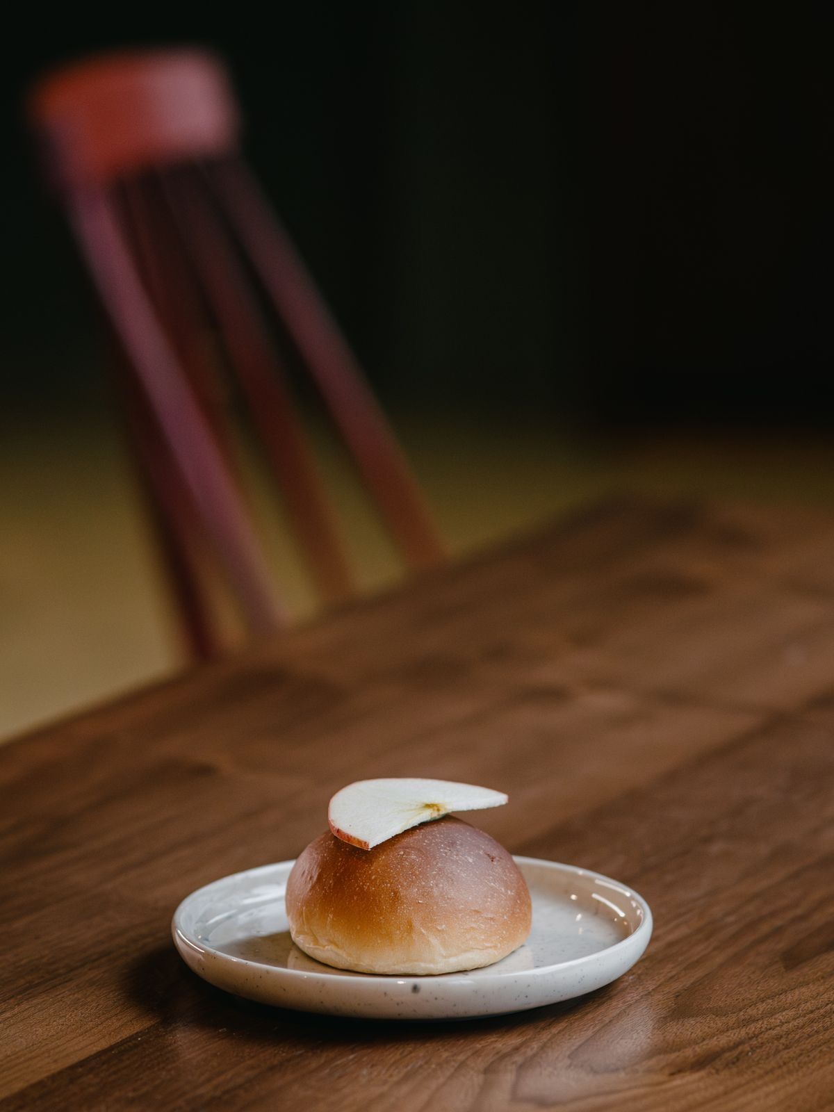 Én bolle på en liten tallerken på et trebord i mørk kafé-stemning