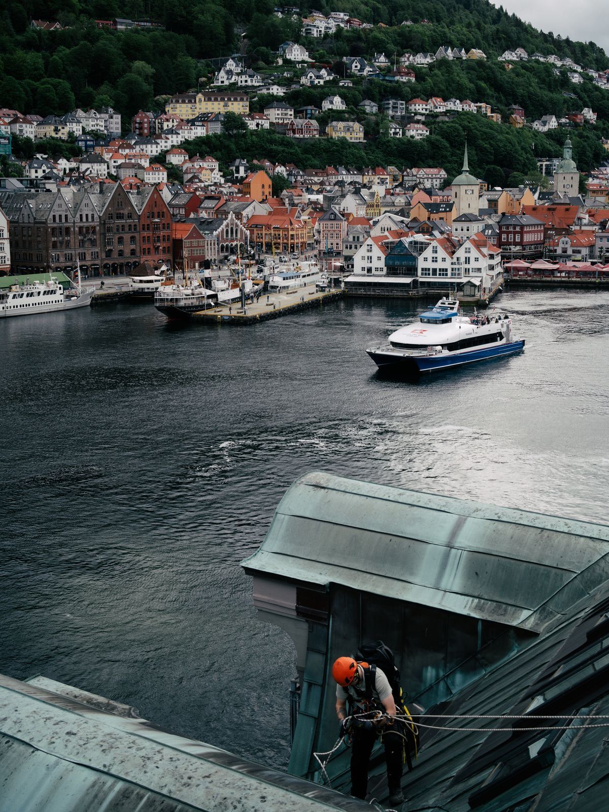 Bergen sett ovenfra med Bryggen og Vågen, en tauarbeider i hjelm på et tak i forgrunnen